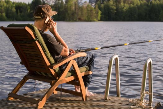 Mature man fishing from wooden pier near cottage on lake in Finland at summer