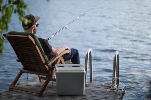 Mature man fishing from wooden pier near cottage on lake in Finland at summer