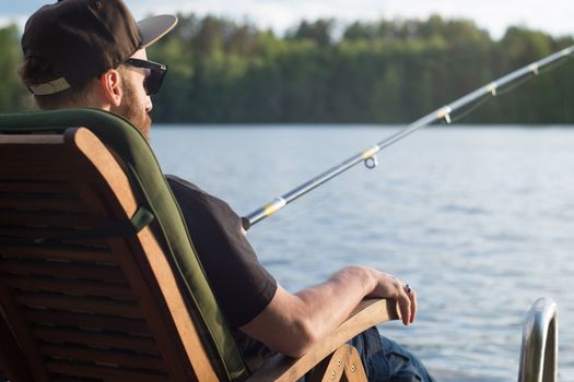 Mature man fishing from wooden pier near cottage on lake in Finland at summer