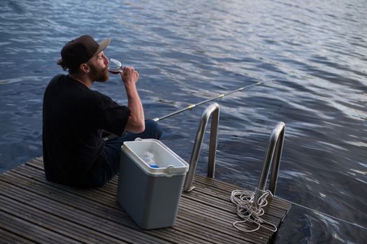 Mature man fishing from wooden pier near cottage on lake in Finland at summer