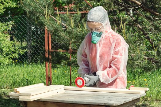 Woman carpenter in respirator, goggles and overalls handles a wooden board with a Angle grinder.