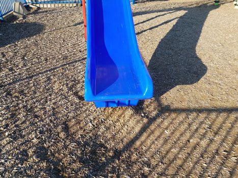 blue plastic slide with brown mulch or wood chips and shadow