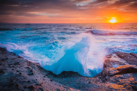 The whoosh of waves as they break on coastal rocks and sent hurtling into the air in dramatic shapes.  Beautiful sunrise colours the sky, with boats out on the horizon