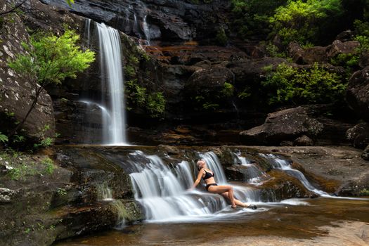 Female sitting in waterfall cascades immersing in nature. One of the nicer waterfalls to visit in Australia