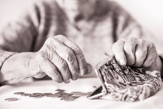 Detailed closeup photo of elderly 96 years old womans hands counting remaining coins from pension in her wallet after paying bills. Unsustainability of social transfers and pension system.