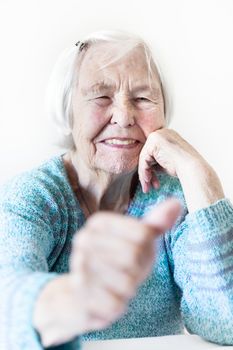 Content 96 years old elderly woman giving a thumb up and looking at camera. Focus on the womans face, thumb out of focus. Old age and the quality of life concept.