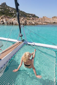 Womanin bikini tanning and relaxing on a summer sailin cruise, lying in hammock of luxury catamaran near picture perfect white sandy beach on Spargi island in Maddalena Archipelago, Sardinia, Italy.