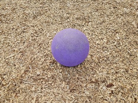 large purple ball or sphere in brown mulch or wood chips