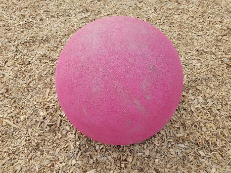 large pink ball or sphere in brown mulch or wood chips