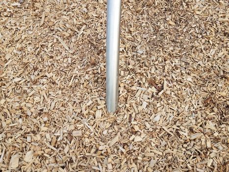 silver metallic bar or rod in brown mulch or wood chips