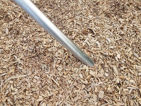 silver metallic bar or rod in brown mulch or wood chips