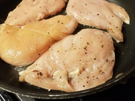 raw chicken breast meat cooking in frying pan with oil