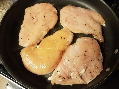 raw chicken breast meat cooking in frying pan with oil