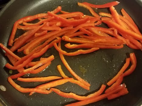sliced red peppers vegetables cooking in frying pan with oil