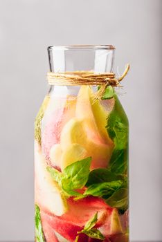 Part of Bottle of Infused Water with Sliced Peach and Basil Leaves. Vertical Orientation.