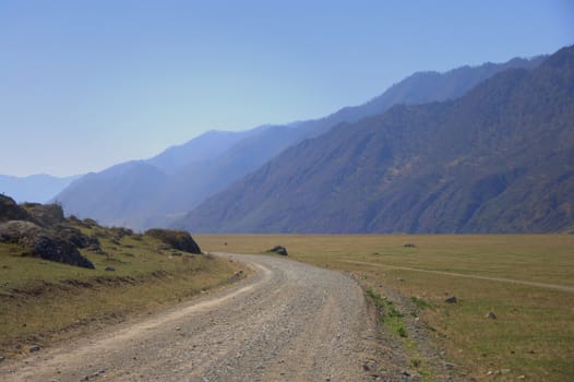 A good dirt road winding at the foot of high mountain ranges. Altai, Siberia, Russia.