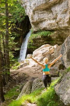 Active woman raising arms inhaling fresh air, feeling relaxed and free in beautiful natural environment under Pericnik waterfall in Vrata Valley in Triglav National Park in Julian Alps, Slovenia.