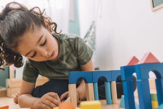 child little girl playing constructions on the floor with wooden building block toys at home or kindergarten, educational toys for creative children