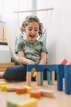 funny little girl playing in the floor with colorful wooden building block toys at home or kindergarten, educational toys for creative children