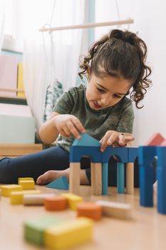 little girl playing concentrated in the floor with colorful wooden building block toys at home or kindergarten, educational toys for creative children