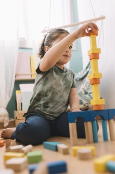 concentrated little girl playing happy in the floor with colorful wooden building block toys at home or kindergarten, educational toys for creative children