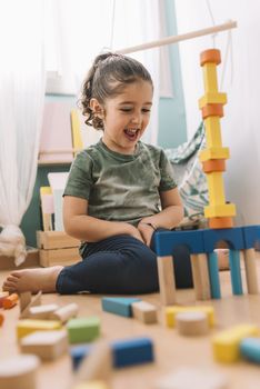 happy little girl playing funny in the floor with colorful wooden building block toys at home or kindergarten, educational toys for creative children