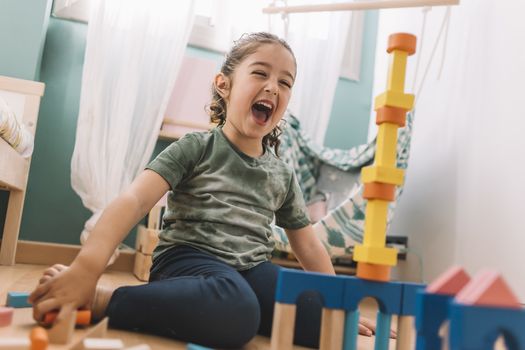 funny little girl laughing while playing happy in the floor with colorful wooden building block toys at home or kindergarten, educational toys for creative children