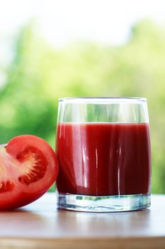 Full glass of tomato juice against nature background