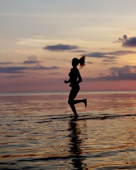 silhouette of a girl run on the beach sand. Shooting against the sun. Sunset over the sea.