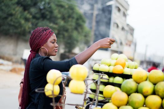 young woman buys fruit at the street market placed on shelves.