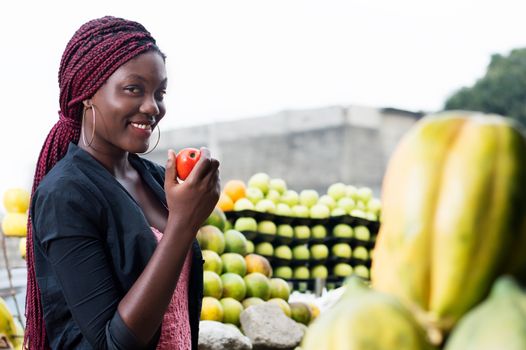 smiling young woman shows a ripe tomato looking at the camera.