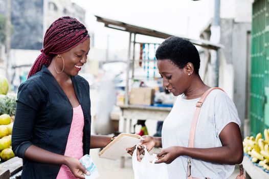 Young happy women at the market looking in a bag containing fruit.