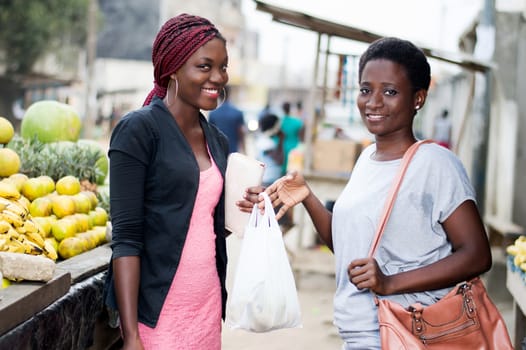 portrait of young smiling women standing in the fruit market holding dryers containing fruit.