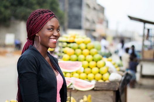 portrait of smiling young woman standing near a table with a bunch of fruit.