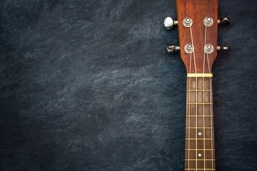 Ukulele on black cement background. Headstock and fret of ukulele parts. Copy space for text. Concept of Hawaiian musical instruments and music lovers.