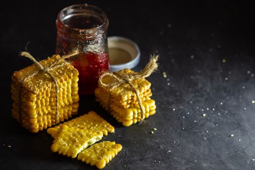 Crackers are tied with hemp rope and strawberry jam bottle on table in dark background.