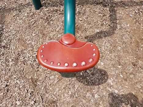 red and metal seat on seesaw or teeter totter with brown wood chips or mulch