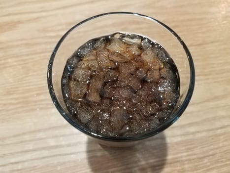 glass of soda beverage with ice on brown table