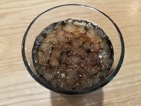 glass of soda beverage with ice on brown table