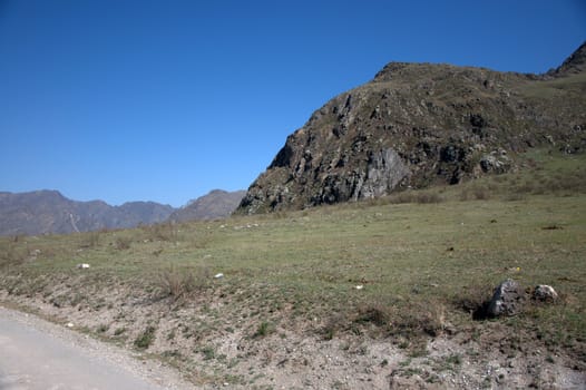 Mountain range near the dirt road on the background of a clear blue sky. Altai, Siberia, Russia.