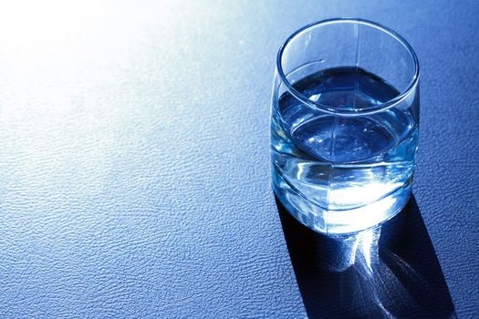 Half glass of water on dark blue background with shadow