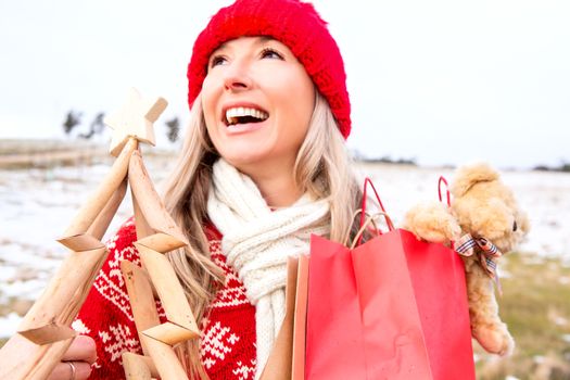 joyous womwn holding timber Christmas tree and gift bags in a snowy landscape.  Blue Mountains, Australia, Christmas, aussie culture, Christmas in July, seasonal