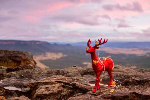 Red glittery reindeer decorated with golden star twinkle lights stands on a cliff edge in Blue Mountains, Christmas season, Christmas in July, Christmas in Blue Mountains.  Shallow dof with copy space.