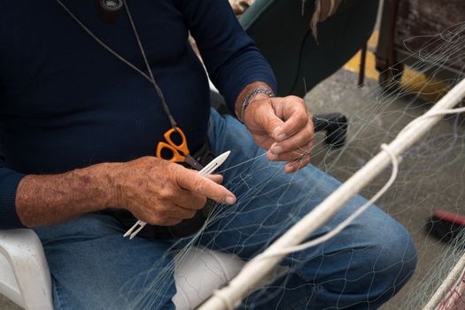 Old fisherman reparing fishing net.