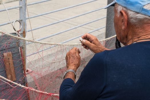 Old fisherman reparing fishing net, sitting with pipe in his mouth.