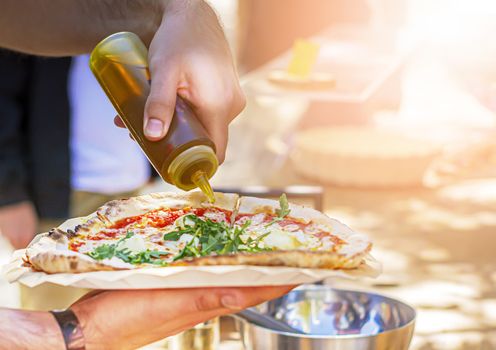 A male pouring olive oil to season a pizza. Italian cuisine. traditional Italian recipe.