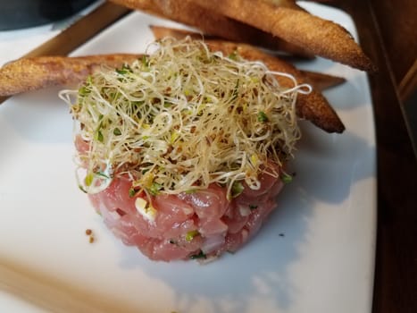 raw tuna tartare on white plate with sprouts and fries