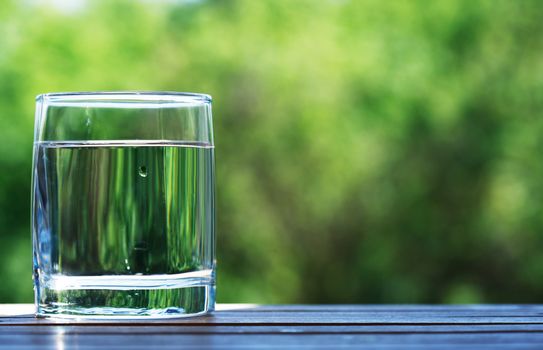 Glass of cold water against nice green nature background
