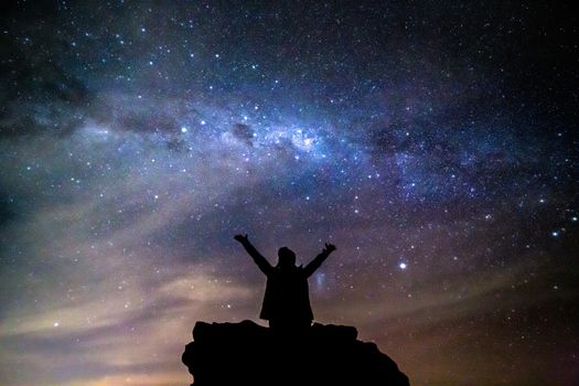 A woman sits on a rock staring deep into the vast universe philosophically reminding oneself of our small place in the cosmos