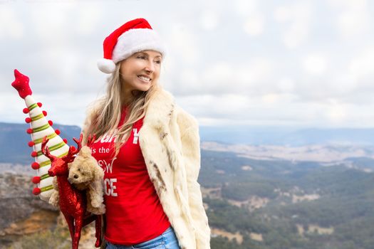 Woman holding some Christmas decorations and or gifts with a beautiful backdrop of Blue Mountains and valley suitable for Christmas themes or Christmas in July winter festival